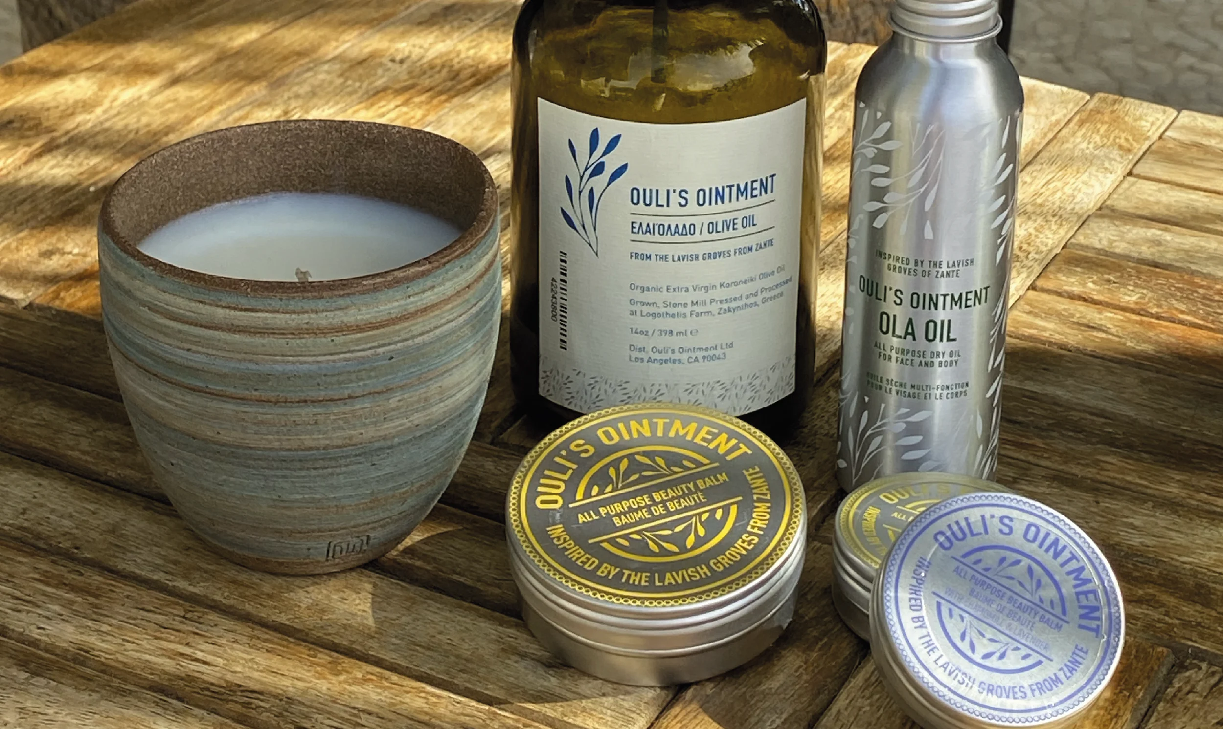 Ouli's Ointment balms, oil and candle arranged on a wooden table.
