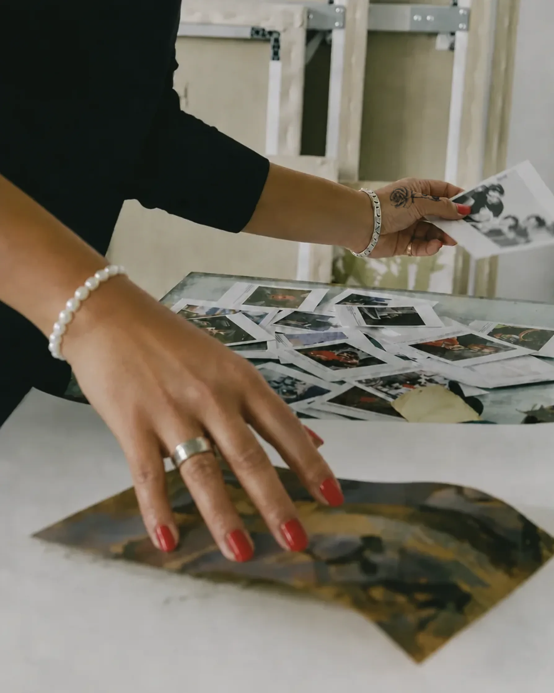 Tattooed hands with red nails arranging photographs on a studio table