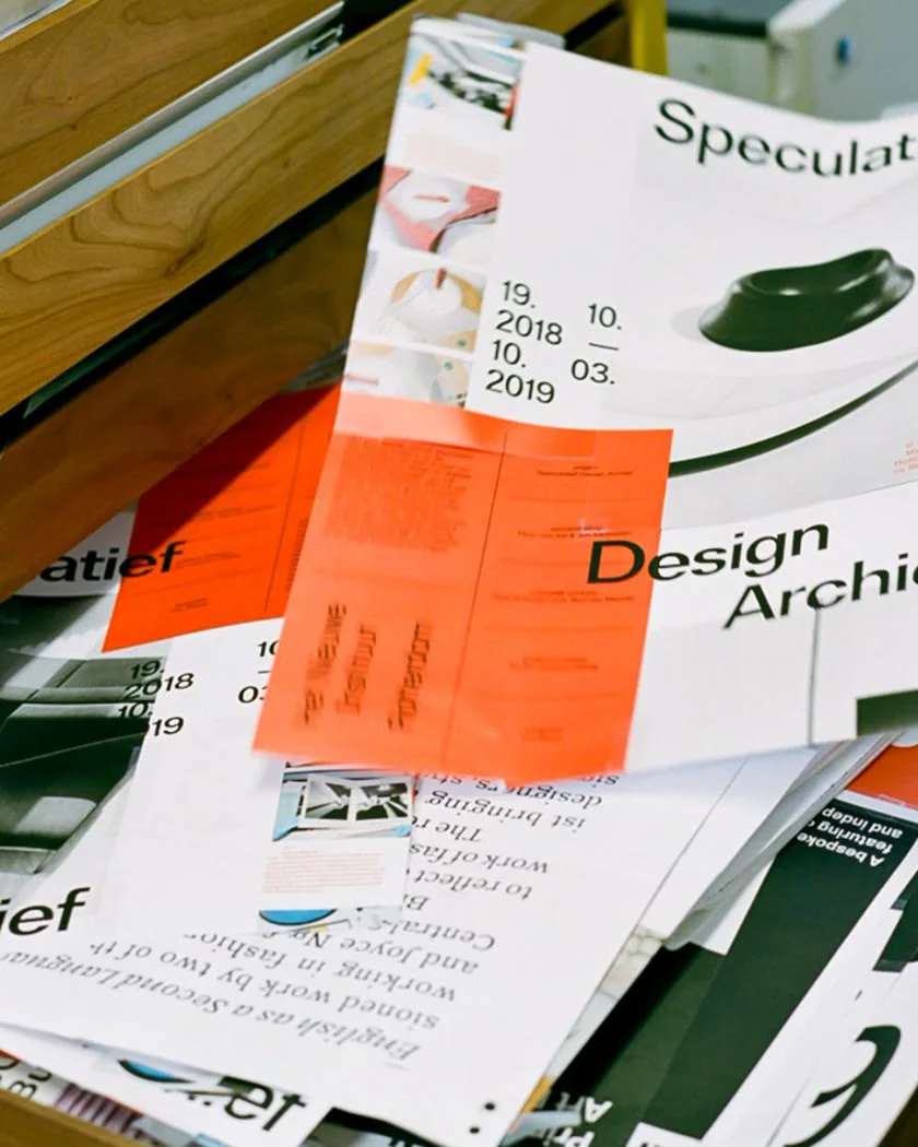 Layered graphic design prints and orange paper studies in a studio drawer